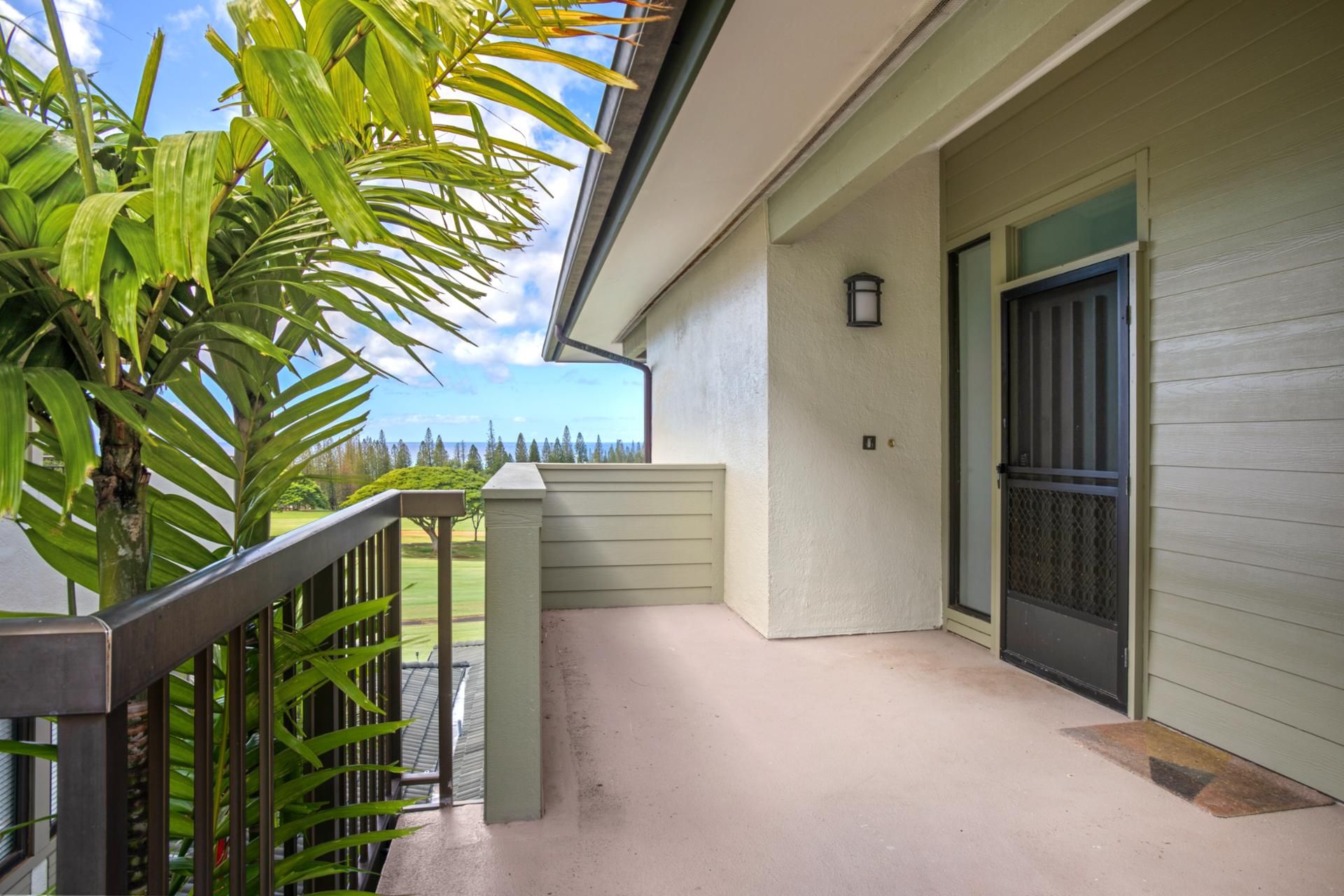 A balcony with a view of a golf course, a door with a security screen, and a small wall-mounted light fixture.