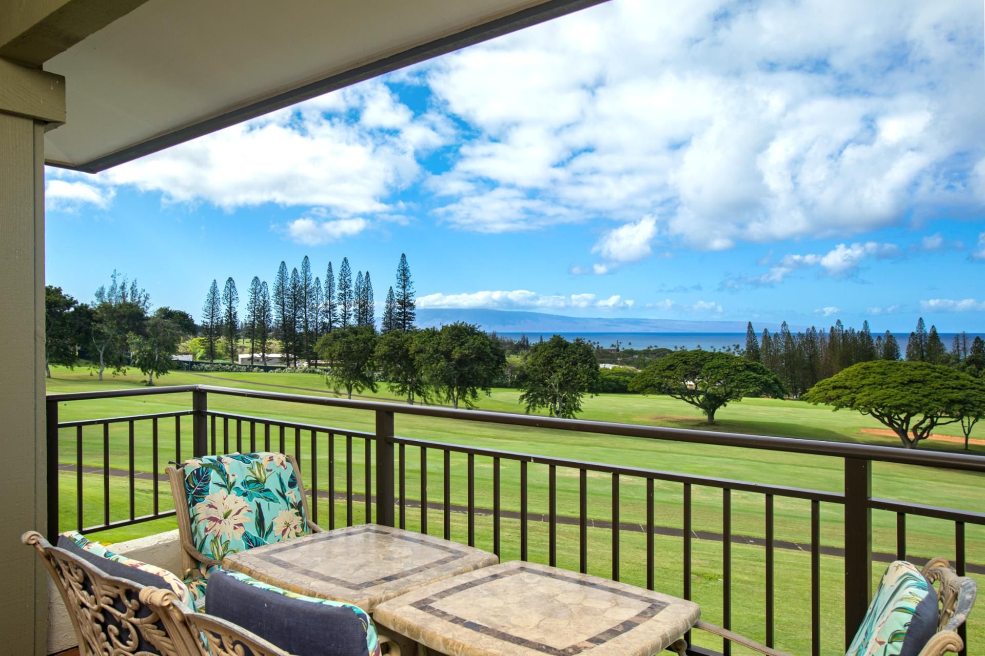 A balcony with a view of a golf course, a table, and two chairs.