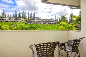 A balcony with wicker chairs, a view of a residential area with multiple buildings and lush greenery.