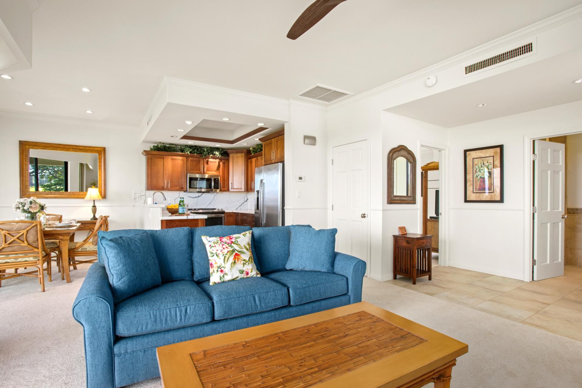 A spacious living room with a blue sofa, wooden coffee table, and a kitchen in the background.