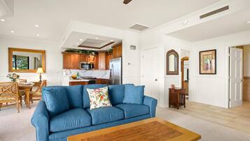 A spacious living room with a blue sofa, wooden coffee table, and a kitchen in the background.