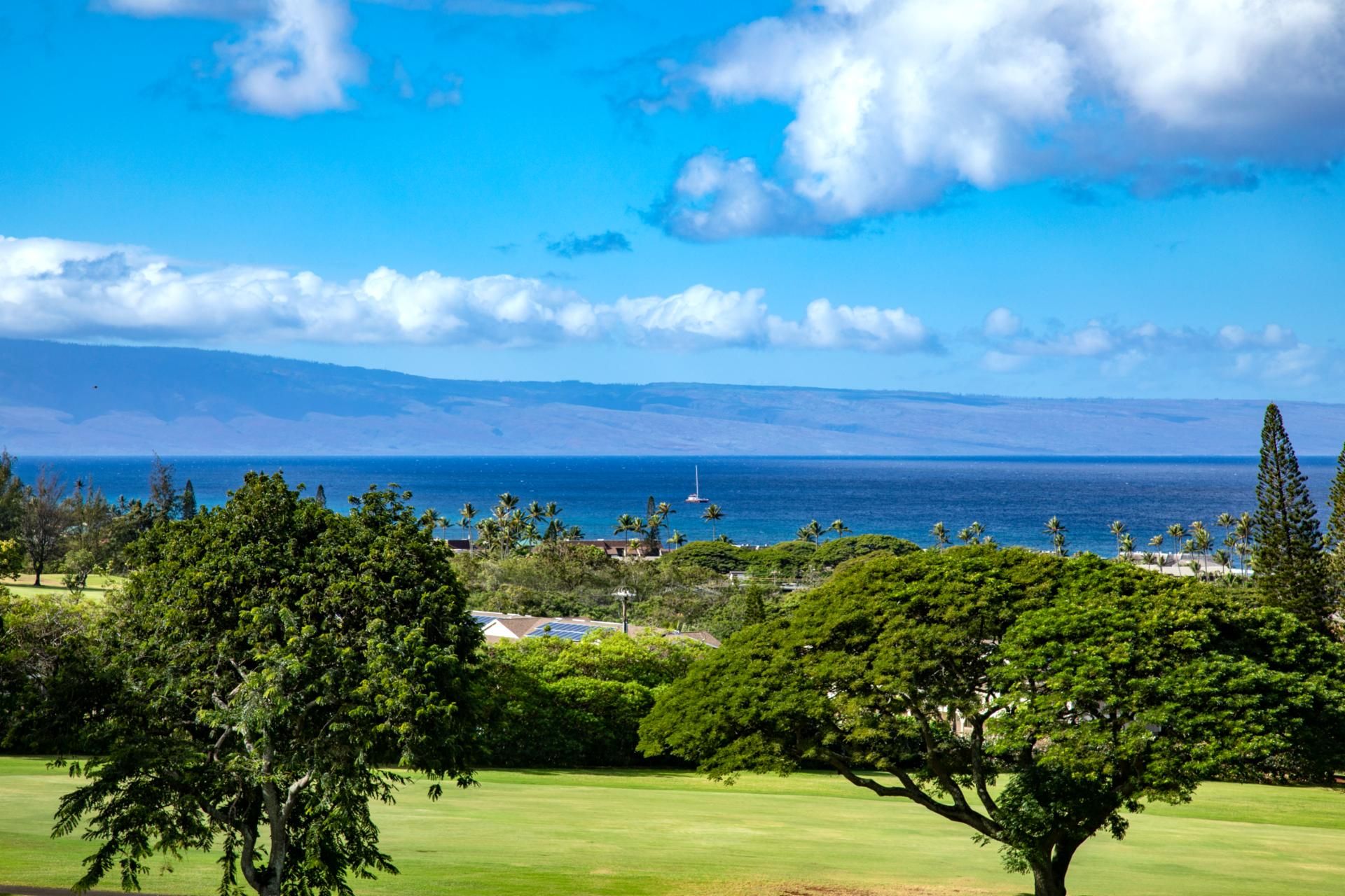 A coastal landscape with a clear view of the ocean, a golf course, and distant mountains.