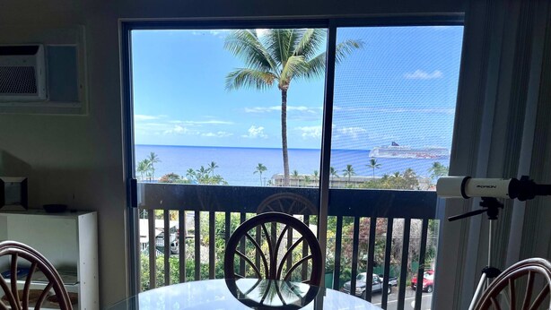 Ein Balkon mit Glastisch und Stühlen, der Blick geht auf die Küste mit Palmen und dem Meer.