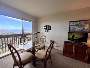 Un balcon avec une table et des chaises en verre, un téléviseur et des tableaux encadrés au mur.