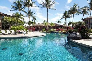 A pool area with lounge chairs, palm trees, and a building in the background. - Honu Harmony | Pools, Golf Privileges, & More (Waikoloa Beach Resort)