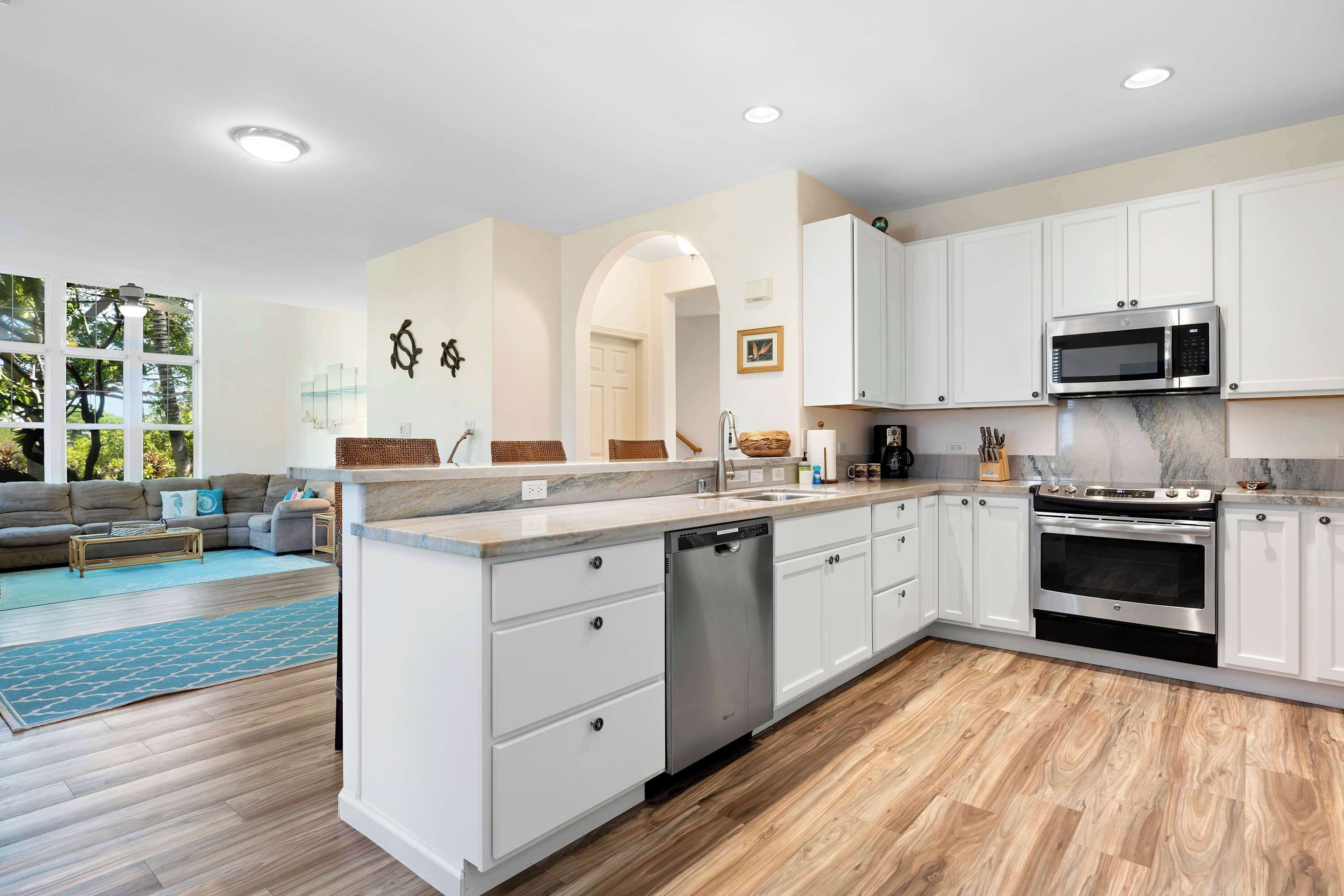 A modern kitchen with white cabinets, stainless steel appliances, and a wooden floor.