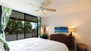 Un dormitorio con cama, ventilador de techo, mesita de noche, lámpara y vistas al exterior.