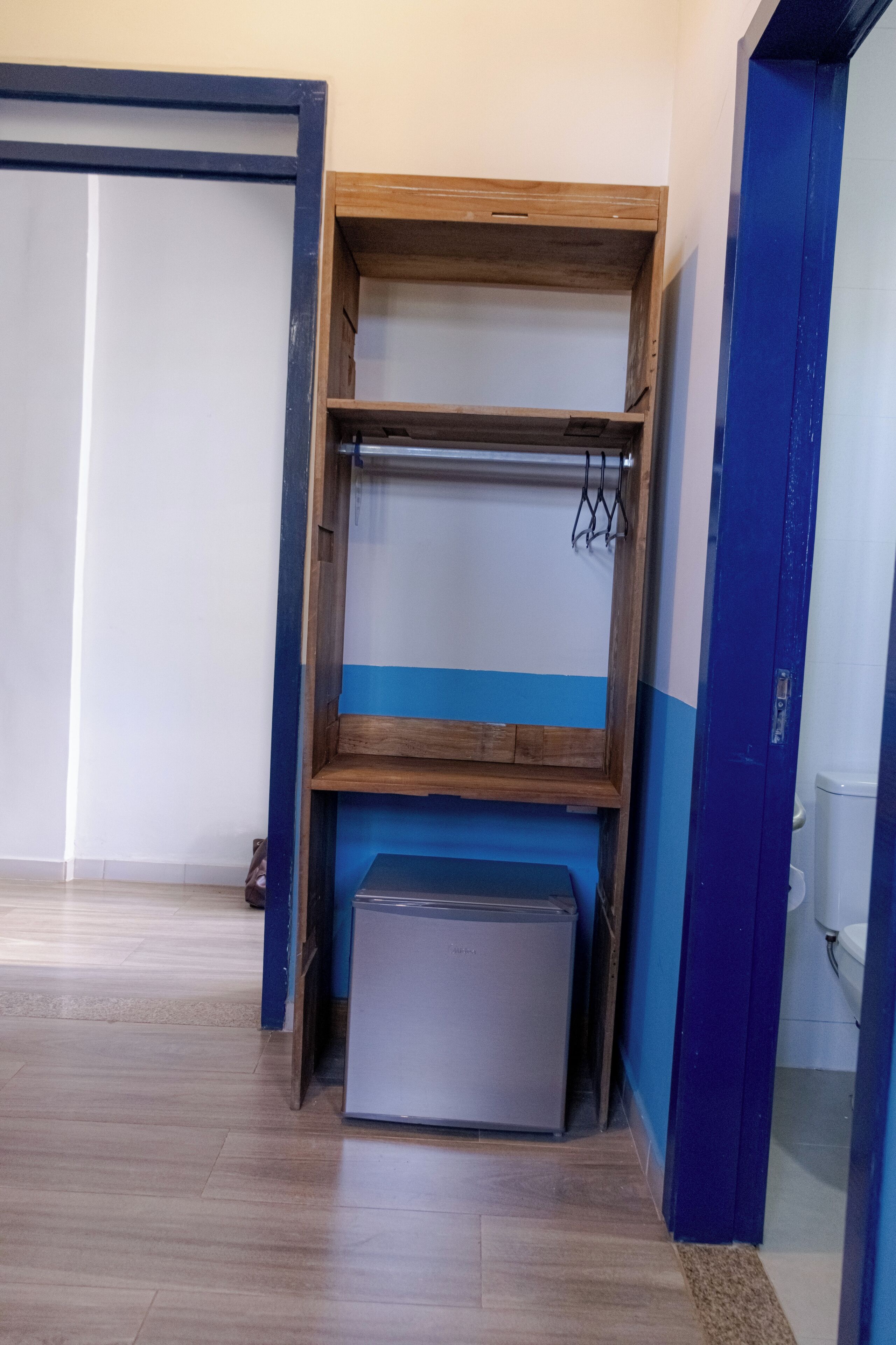 A room with a wooden shelf unit, a small refrigerator, and a blue door.