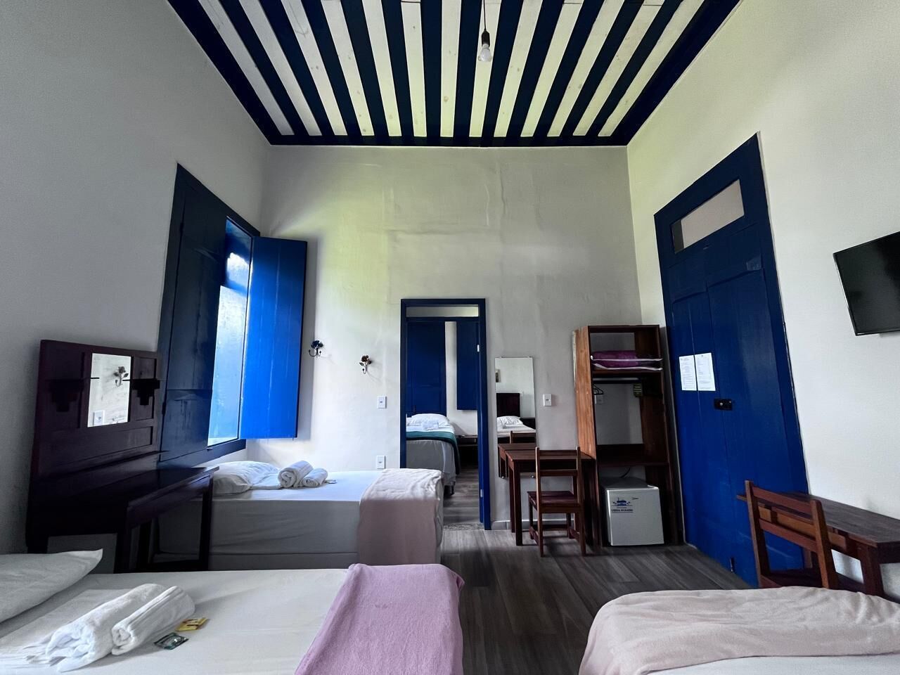 Habitación de hotel con dos camas, un escritorio, una silla, un armario y un televisor.