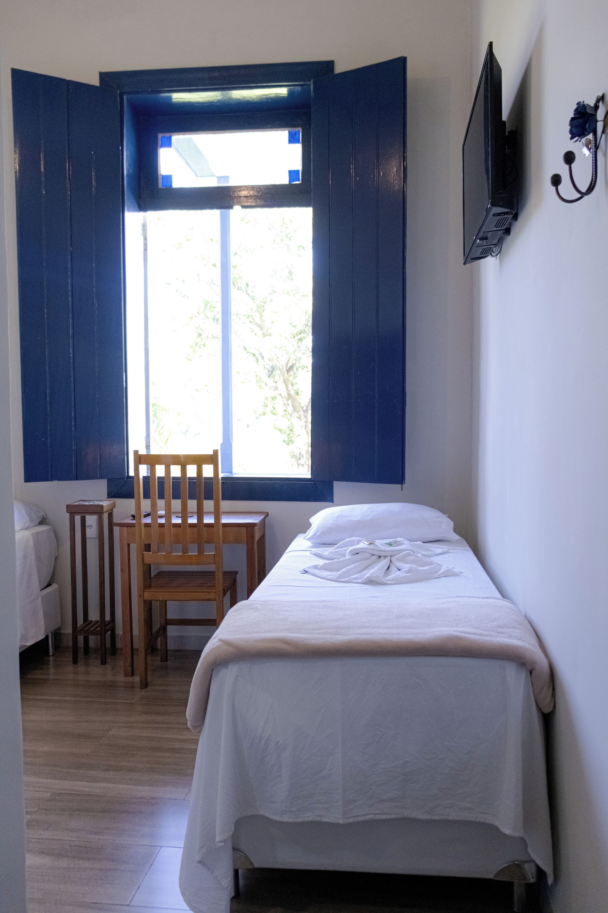 Un dormitorio con una cama, una silla, una mesita y un televisor montado en la pared.