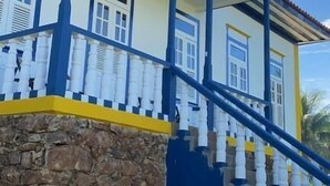 A two-story building with a stone foundation, a balcony with white balustrades, and a blue and yellow color scheme. - Pousada Usina Paraíso (Astolfo Dutra)