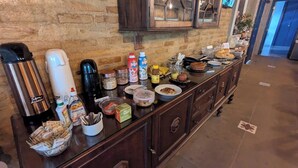 A buffet setup with various food items and condiments on a counter against a brick wall. - Pousada Usina Paraíso (Astolfo Dutra)