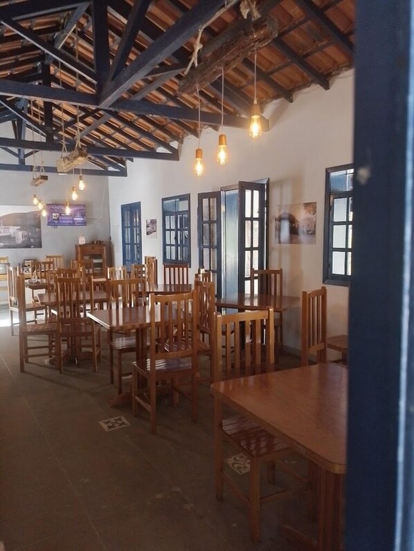 A dining area with wooden tables and chairs, a high ceiling with exposed beams, and hanging light fixtures.