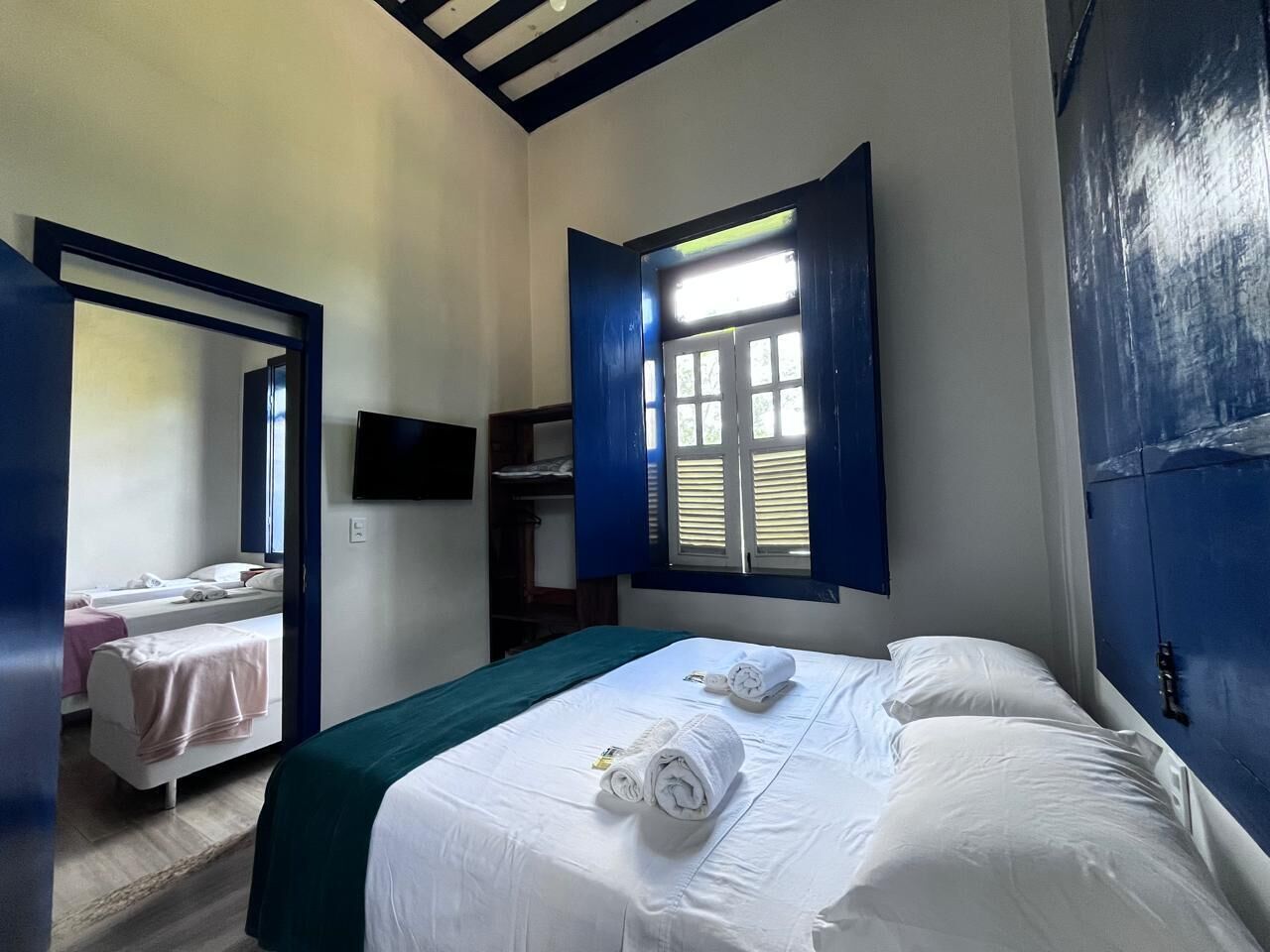 A room with a bed, a smaller bed, a TV, and a window with shutters.