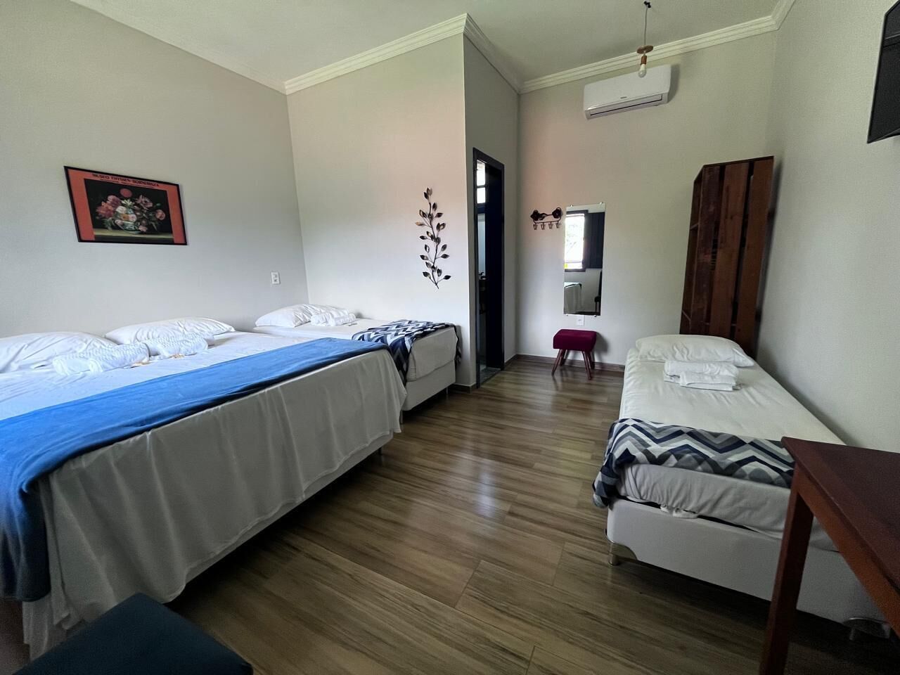 Una habitación con dos camas, suelo de madera, una mesita y un aire acondicionado instalado en la pared.