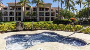 Un hotel con un jacuzzi rodeado de palmeras y un césped bien cuidado.