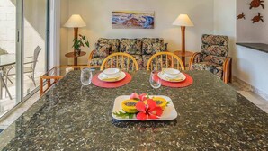 A dining area with a marble table, chairs, and a tropical-themed painting on the wall. - Kona White Sands A4 | Romantic Ocean View! (Kailua Kona)
