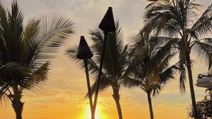 A beachside view with palm trees, a sunset, and people relaxing.