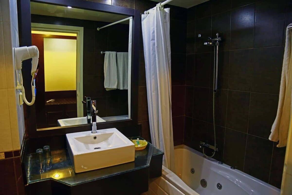 A bathroom with a large mirror, a white sink, a shower, and a hairdryer.