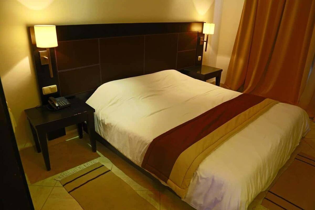 A hotel room with a large bed, two bedside tables, a telephone, and a lamp on each table.