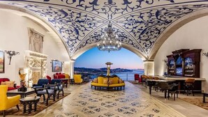 A luxurious lobby with a high ceiling, ornate blue and white ceiling design, a chandelier, a bar area, and a view of the cityscape. - 4BD Oceanfront Unit Vista Encantada Cabo (Cabo San Lucas)