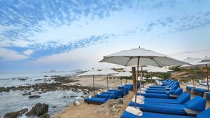 A beachside lounge area with rows of blue lounge chairs and white umbrellas, overlooking the ocean. - 4BD Oceanfront Unit Vista Encantada Cabo (Cabo San Lucas)