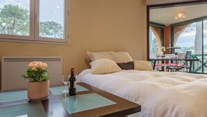 A hotel room with a bed, a table with a vase of flowers, and a view of the outdoors. - Le Landais - Wifi - Loggia - Plage (Tarnos)