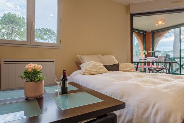A hotel room with a bed, a table with a vase of flowers, and a view of the outdoors.