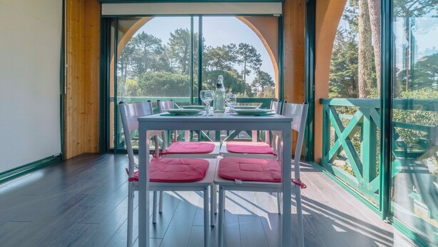 A dining area with a table set for four, large windows, and a view of trees. - Le Landais - Wifi - Loggia - Plage (Tarnos)