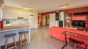 A modern kitchen with white cabinets, a microwave, and a wooden countertop. There is a red sofa and a glass table with a red chair. - Le Landais - Wifi - Loggia - Plage (Tarnos)