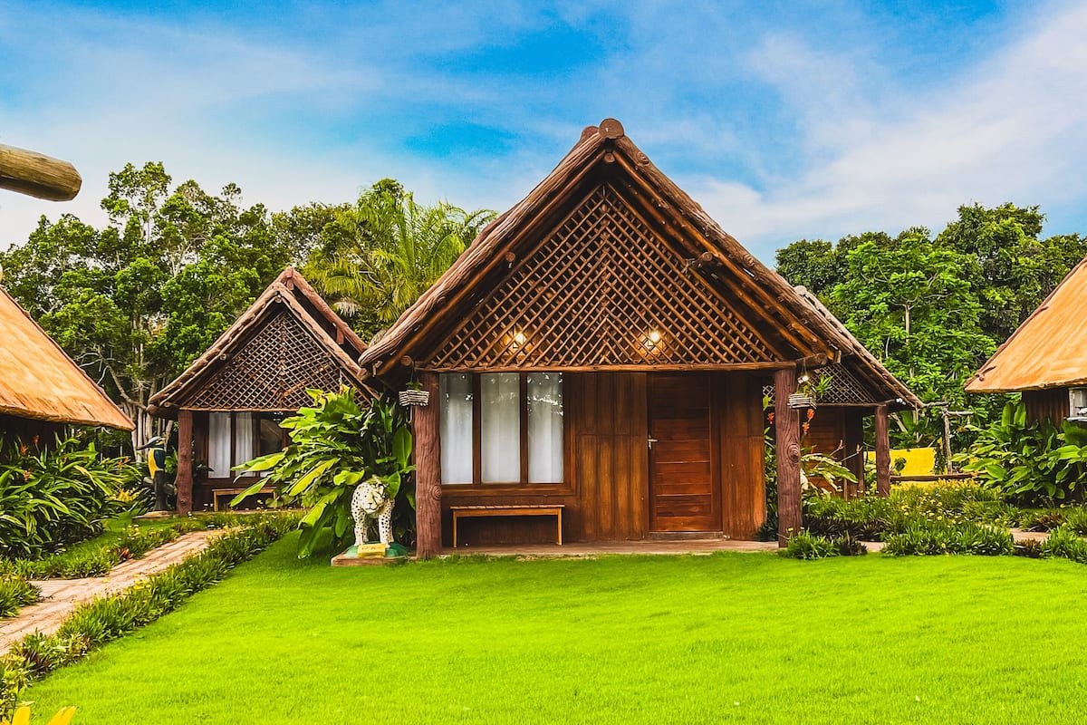A bungalow-style resort with a thatched roof and wooden walls, surrounded by lush greenery and a well-maintained lawn.