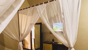 A room with a bed under a canopy, a small table with a lamp, and a television on a stand. - Hotel Chalés do Santuario  (Santa Cruz Cabralia)