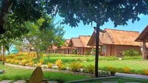 A row of wooden cabins with thatched roofs, surrounded by well-maintained lawns and tropical plants. - Hotel Chalés do Santuario  (Santa Cruz Cabralia)