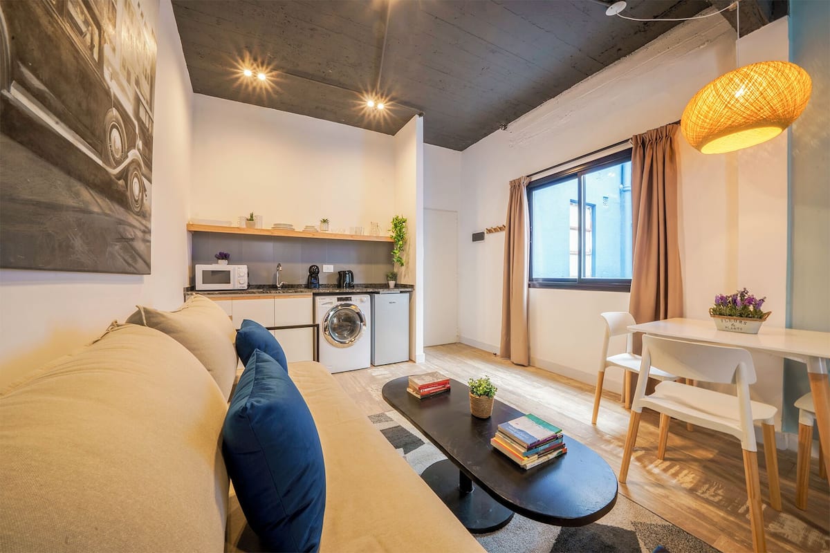 A compact living space with a sofa, a dining table, a kitchen area, and a large window.