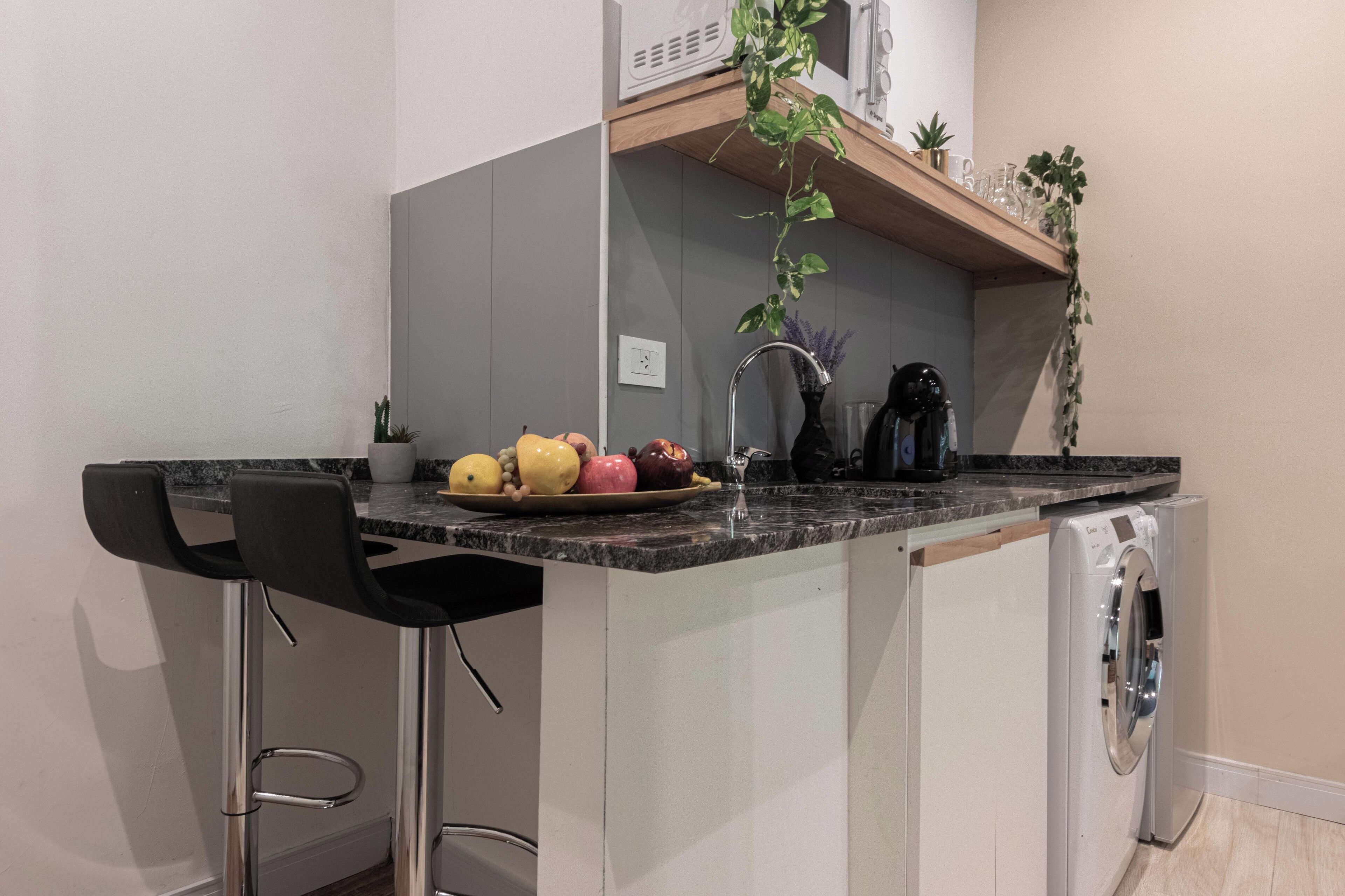Eine kompakte Küche mit integrierter Waschmaschine, Obstschale und einer kleinen Bar mit Hockern.