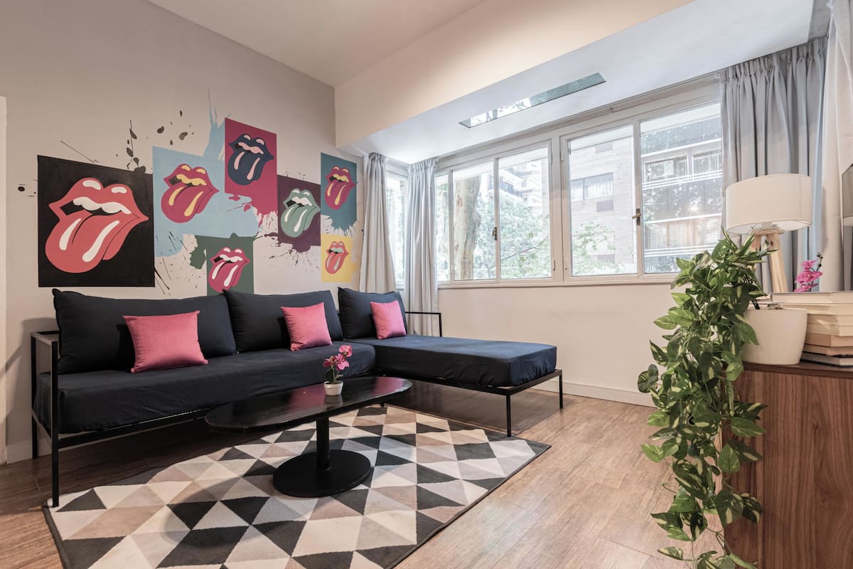 A modern living room with a black sectional sofa, a geometric rug, and a large window with curtains.