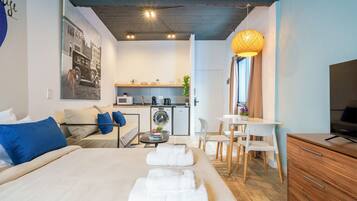 A modern hotel room with a large bed, a kitchenette, a dining area, and a TV.