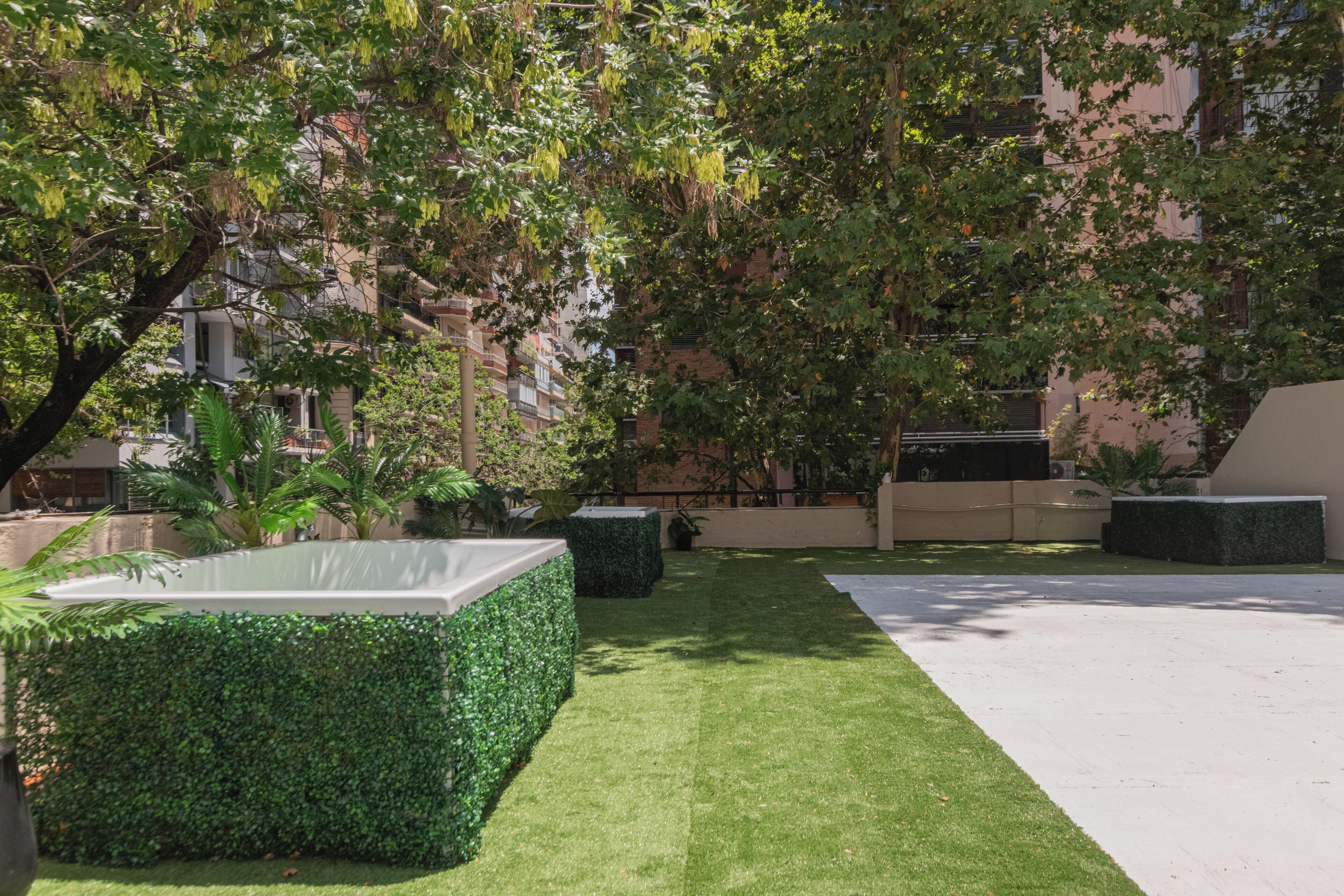 A courtyard with artificial grass, neatly trimmed hedges, and a variety of potted plants.