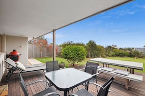 A covered patio with a barbecue grill, outdoor seating, and a view of a backyard. - Surfside Serenity (Anglesea)
