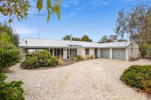 A modern two-story house with a gravel driveway, surrounded by native vegetation and trees.