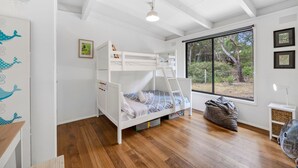 Une chambre avec un lit superposé, une fenêtre, un plancher en bois et un ventilateur de plafond.