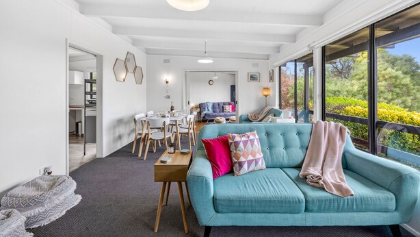 Un salon moderne avec un canapé de couleur turquoise, un coin repas et une vue sur la verdure grâce à de grandes fenêtres.