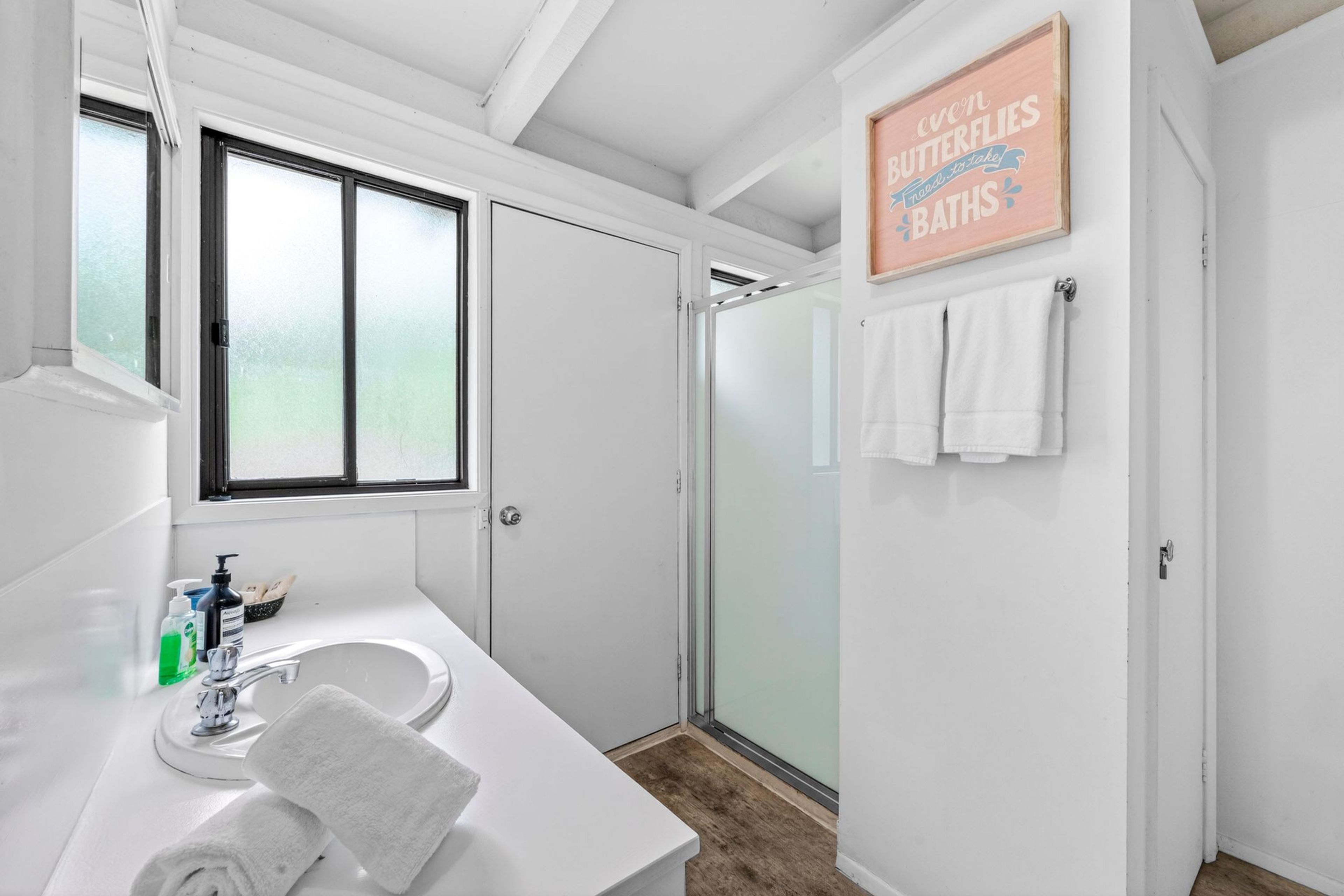 A modern bathroom with a large window, a shower, and a sign that reads 'even butterflies need to take baths.'