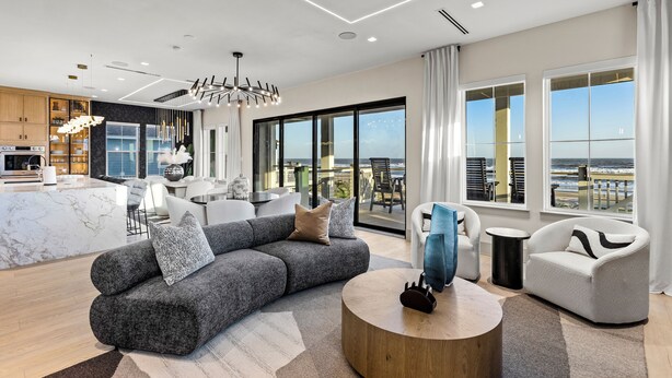 Uma sala de estar moderna com um sofá modular cinza, uma mesa de centro redonda e vista para o oceano através de grandes janelas.