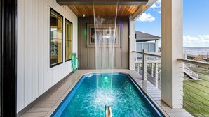 Piscina com cascata, rodeada por um deck de madeira e vista para o oceano.