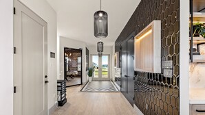 Um corredor moderno com piso de madeira, parede com padrão geométrico e luminária pendente.