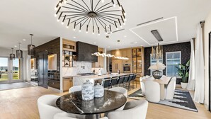 Uma cozinha moderna com ilha central, iluminação pendente e um espaço de refeições com mesa redonda.