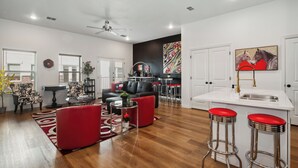 A modern living room with a black leather sofa, red chairs, a coffee table, and a kitchen area with a white countertop and red bar stools. - Walk to the Arlington stadiums from this Luxurious Condo w/ Premium Amenities! Rooftop Retreat w views of stadiums, private garage, gourmet kitchen & gated entry. Book Now to stay at the New Ruby Lux Skyline Retreat  in the Heart of the Arlington! (ARLINGTON)