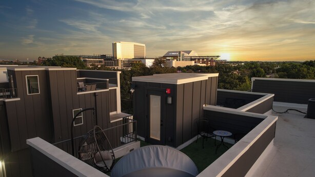 A rooftop terrace with a covered seating area, a small table, and a view of the city skyline at sunset. - Walk to the Arlington stadiums from this Luxurious Condo w/ Premium Amenities! Rooftop Retreat w views of stadiums, private garage, gourmet kitchen & gated entry. Book Now to stay at the New Ruby Lux Skyline Retreat  in the Heart of the Arlington! (ARLINGTON)