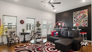 A living room with a black leather sofa, a glass coffee table, a red and white patterned rug, and a ceiling fan. - Walk to the Arlington stadiums from this Luxurious Condo w/ Premium Amenities! Rooftop Retreat w views of stadiums, private garage, gourmet kitchen & gated entry. Book Now to stay at the New Ruby Lux Skyline Retreat  in the Heart of the Arlington! (ARLINGTON)